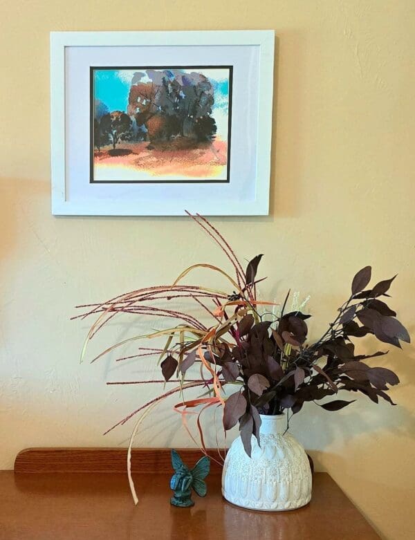 A vase of flowers on the table in front of a picture.