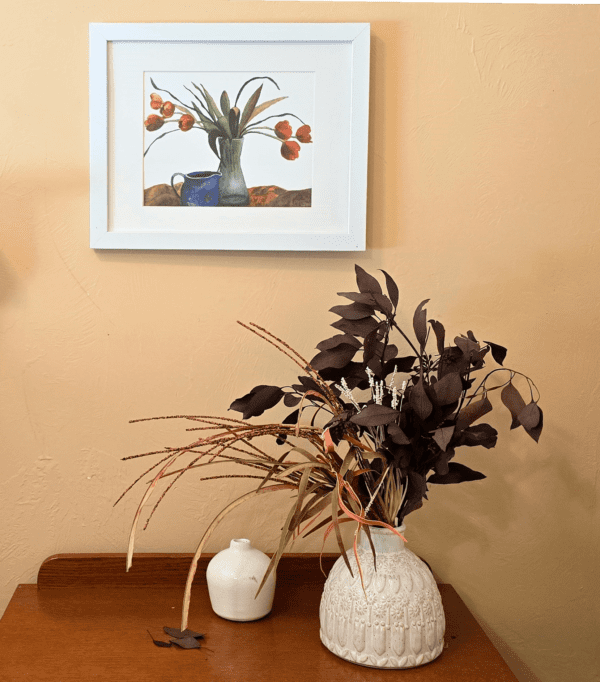 A vase of flowers on the table in front of a picture.