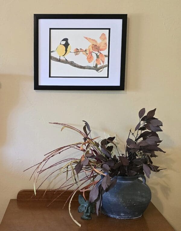 A picture of a bird on the wall above a plant.