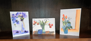 Three paintings of flowers are on a table.