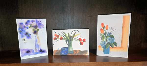 Three paintings of flowers are on a table.