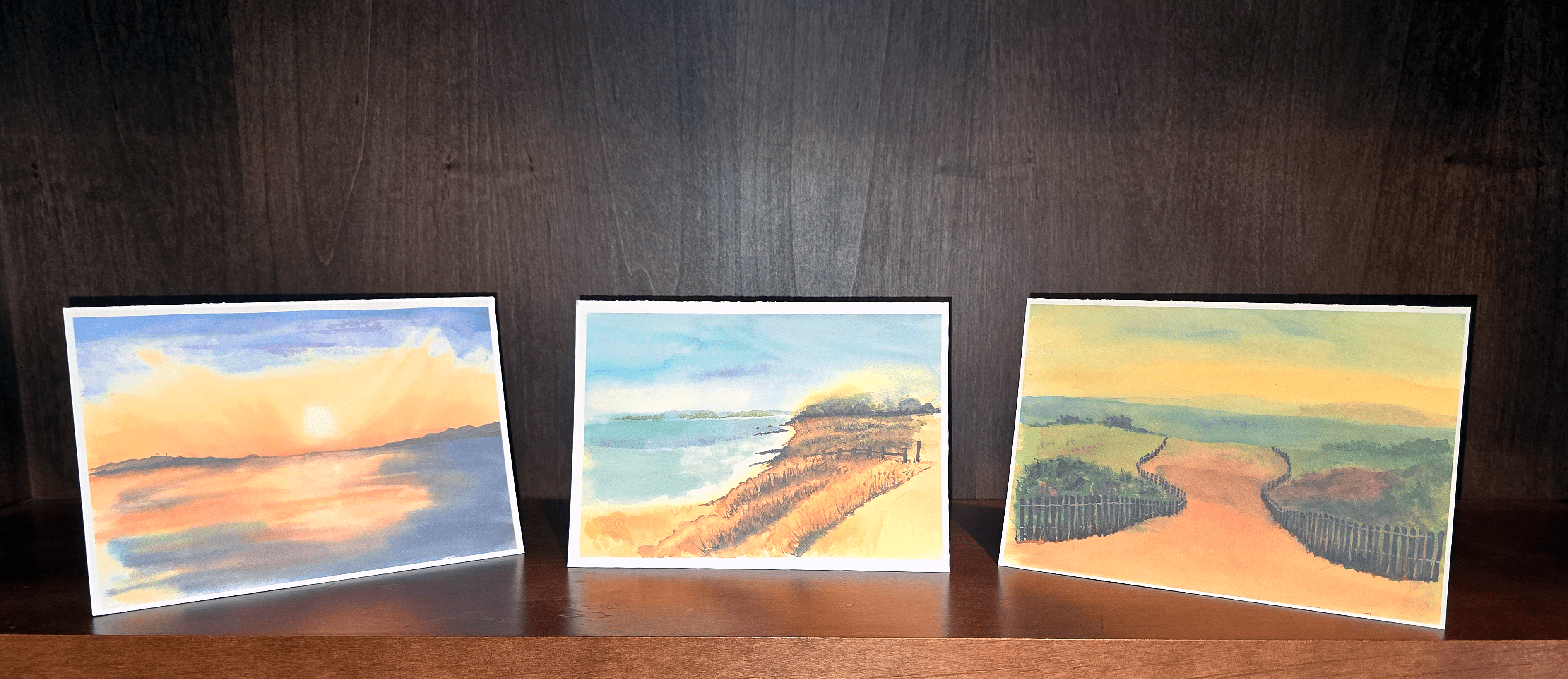 Three paintings of a beach and ocean are on display.