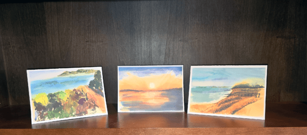 Three paintings of a beach are on display.