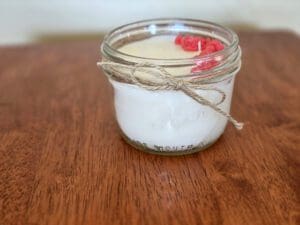 Candle in glass jar on wooden surface.